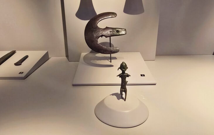 İznik Müzesi’nde sergilenen Tunç Çağı’na ait bronz idol figürü ve hilal biçimli bronz savaş aleti örneklerinin vitrindeki detaylı görünümü.